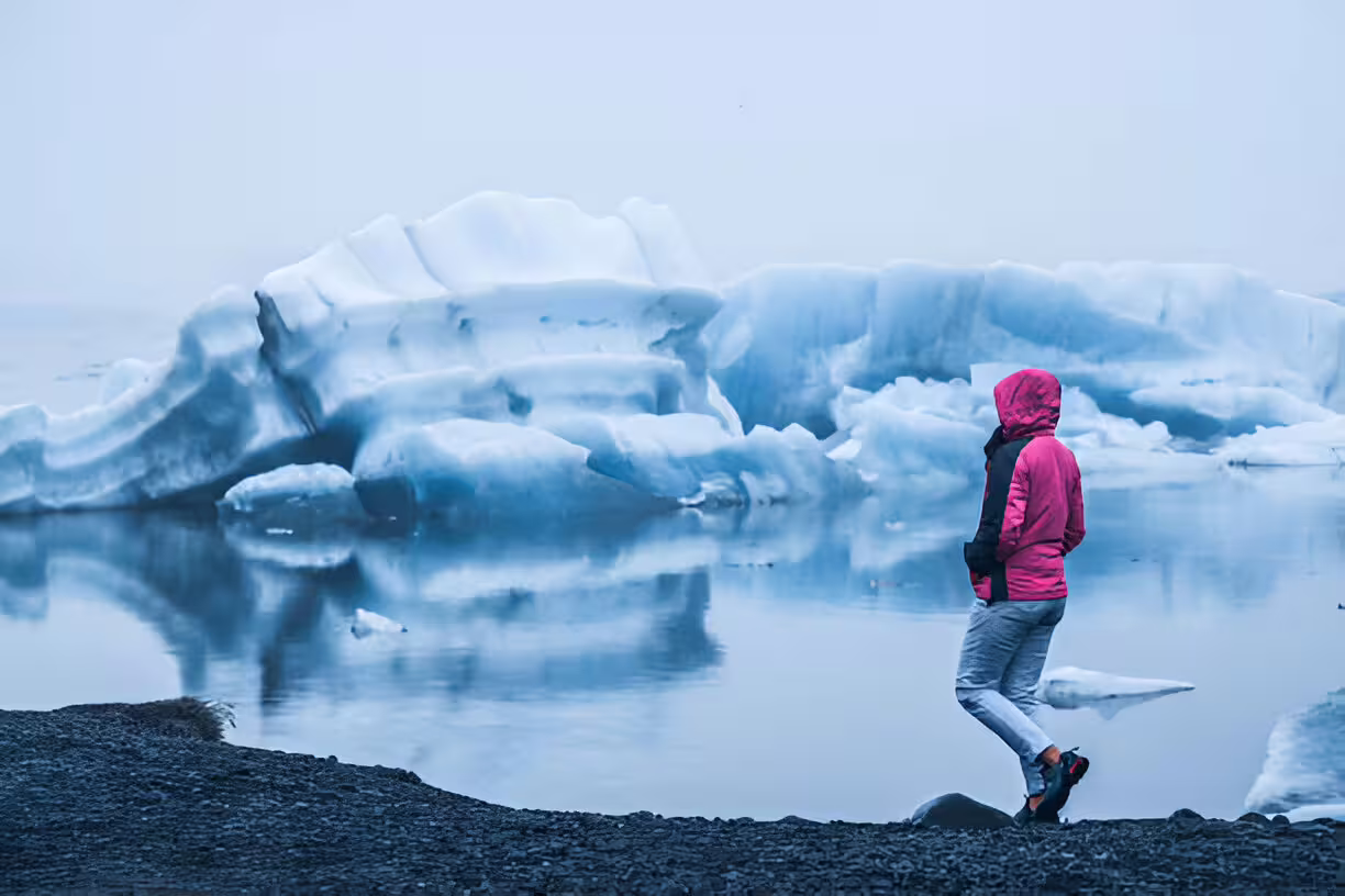 Traveler in pink jacket standing before floating icebergs at Jokulsarlon Glacier Lagoon, Iceland