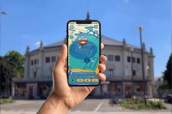 Hand holding smartphone with Jules Verne walking tour app map in front of historic Amiens building