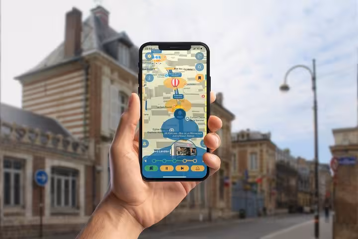 Hand holding smartphone displaying Jules Verne walking tour app map in Amiens city street