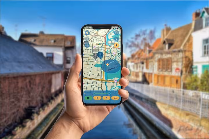 Hand holding smartphone displaying Jules Verne walking tour app map in Amiens canal district