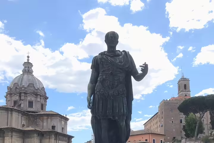 Bronze statue of Julius Caesar with Roman church dome and ancient buildings in Rome