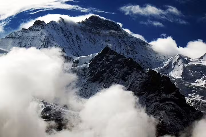 Snow-capped Jungfrau mountain peaks emerging through dramatic clouds under deep blue sky, Switzerland