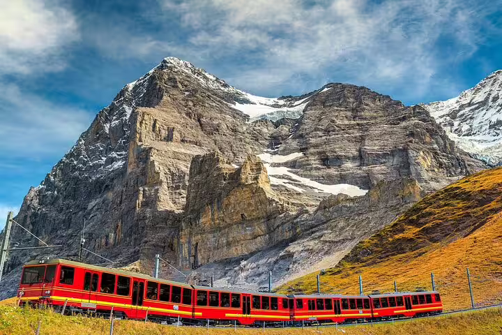 Red Jungfrau railway train passing through alpine meadows beneath the Eiger mountain, Switzerland
