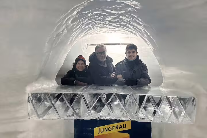 Visitors enjoying the Ice Palace at Jungfraujoch, standing behind a decorative ice sculpture in a gleaming tunnel.