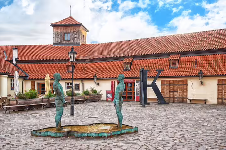 Kafka Museum courtyard in Prague with two bronze urinating statues fountain and red-roofed building