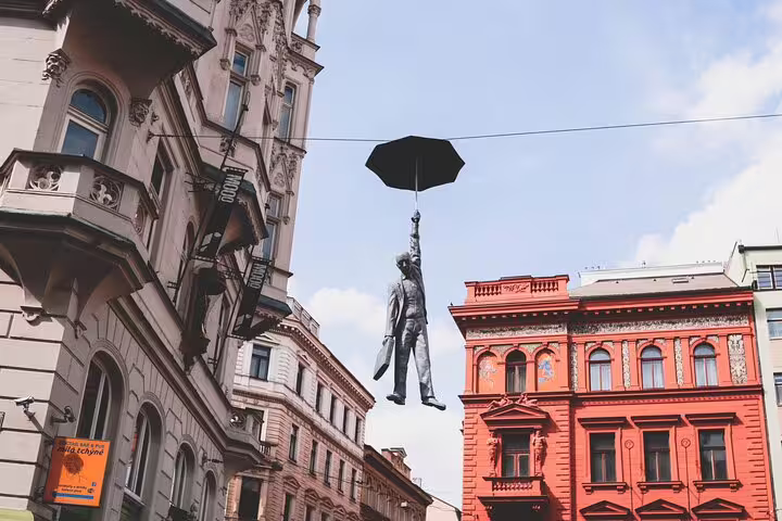 Man hanging from umbrella sculpture suspended between historic Prague buildings
