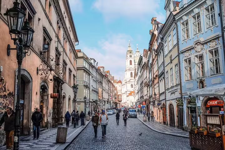 Cobblestone street in Prague's Old Town with historic baroque buildings and St. Nicholas Church in background