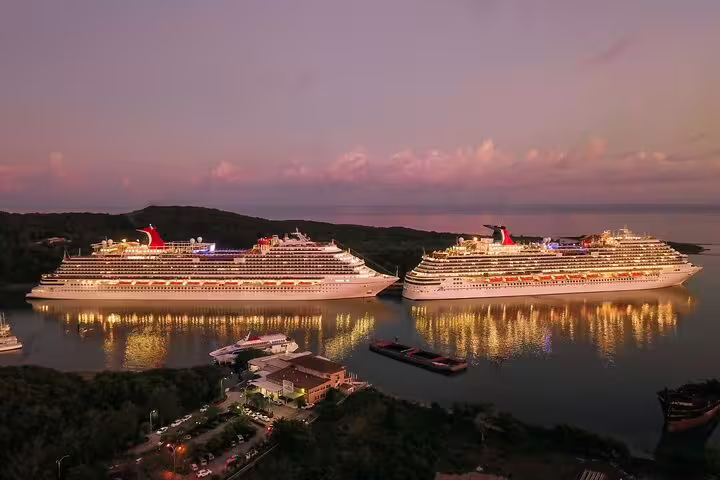 Two large cruise ships docked at Kai Tak Cruise Terminal Hong Kong glowing beautifully at sunset over calm waters.