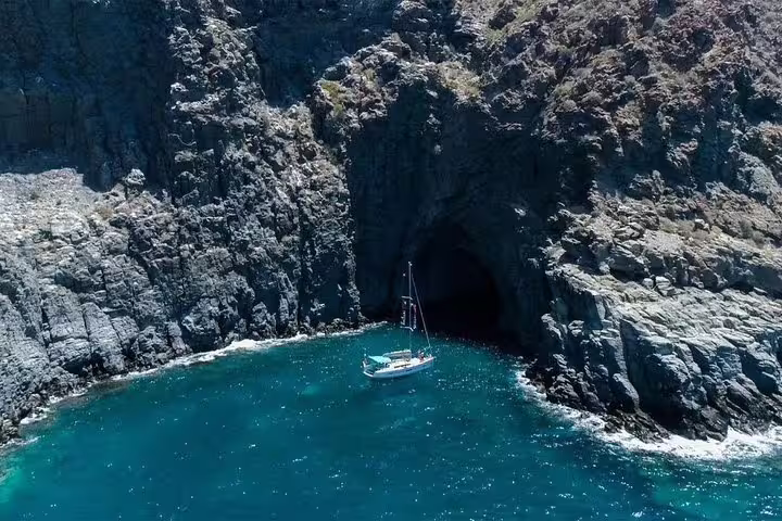 Kailani Sailing Yacht anchored near a stunning sea cave, perfect for exploring marine life on a dolphin and whale tour.