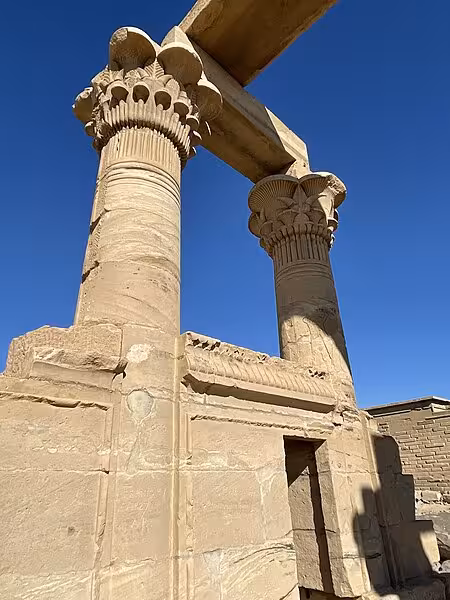 Ancient Egyptian columns with ornate floral capitals at Kalabsha Temple, Aswan, against a clear blue sky