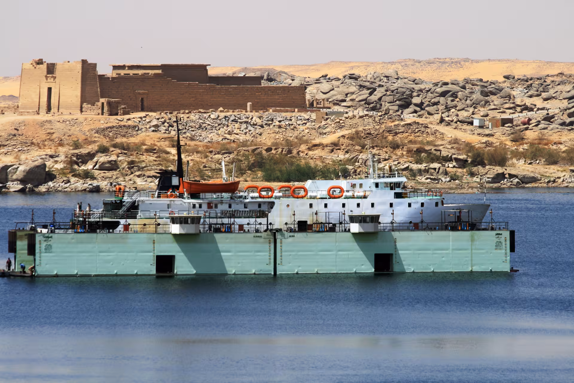 Ferry boat on Lake Nasser with ancient Kalabsha Temple ruins and rocky desert landscape in Aswan, Egypt