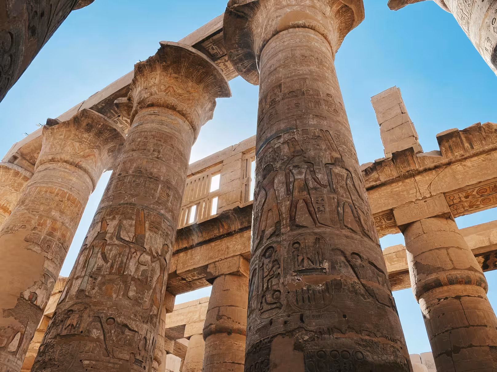 Massive hieroglyph-covered columns at Karnak Temple, Luxor, viewed from below against blue sky