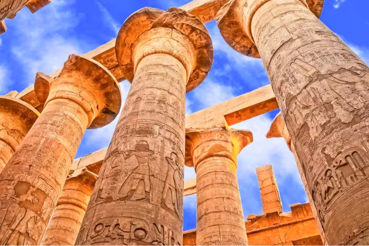 Upward view of Karnak Temple hieroglyphic columns under blue sky, highlight of full-day Luxor tour itinerary