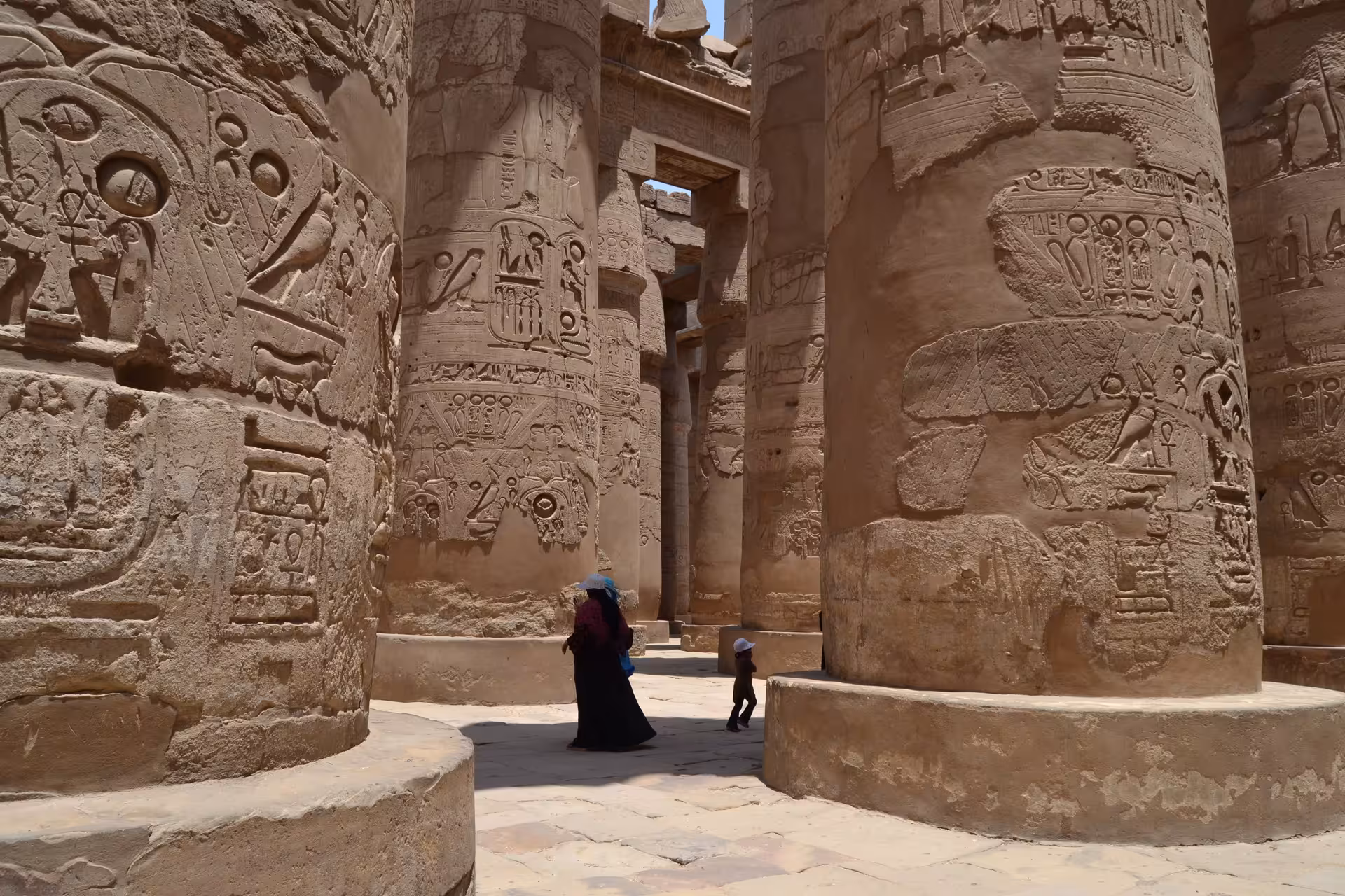 Tourists walking among massive hieroglyph-covered columns in Karnak Temple, Luxor, Egypt