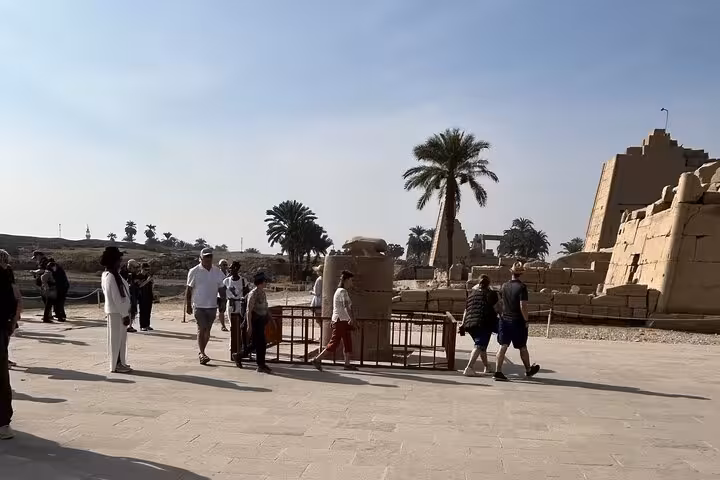 Visitors walking near Karnak Temple complex in Luxor on Hurghada tour, palm trees and ancient stone blocks