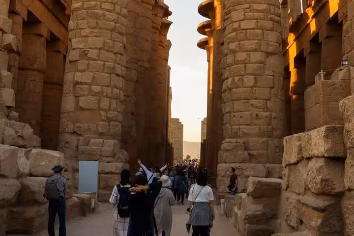 Group walking between massive Karnak Temple pillars at sunset, Comfort Luxor trip from Hurghada with King Tut tomb