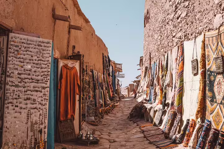 Market lane at Kasbah Ait Benhaddou lined with colorful Berber carpets on a private Marrakech day tour