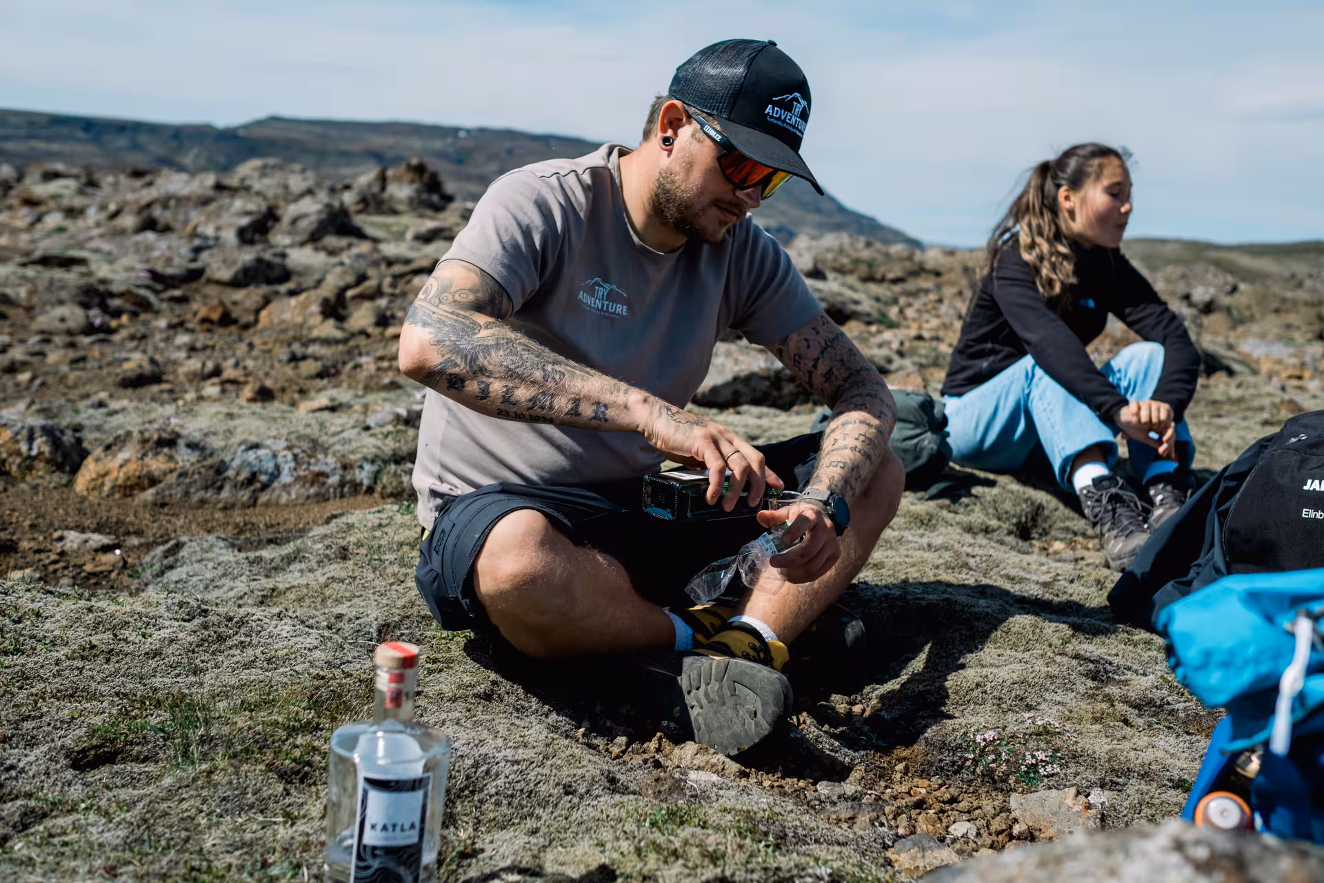 Guide pouring Katla gin shots on volcanic rocks during Iceland geothermal valley tour near Hengill
