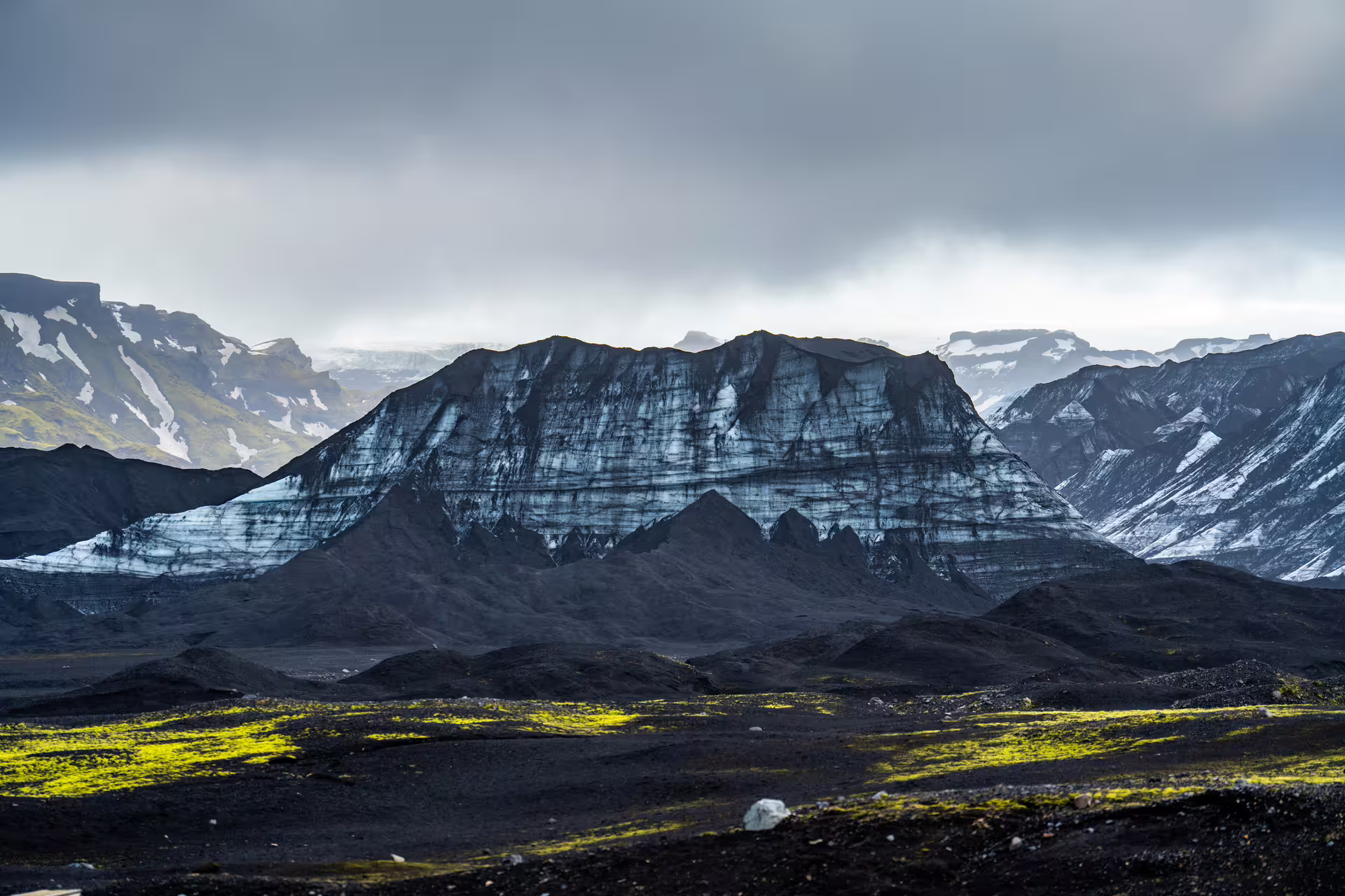 Black volcanic landscape with glacier-covered flat-topped mountain and green moss on Iceland's south coast