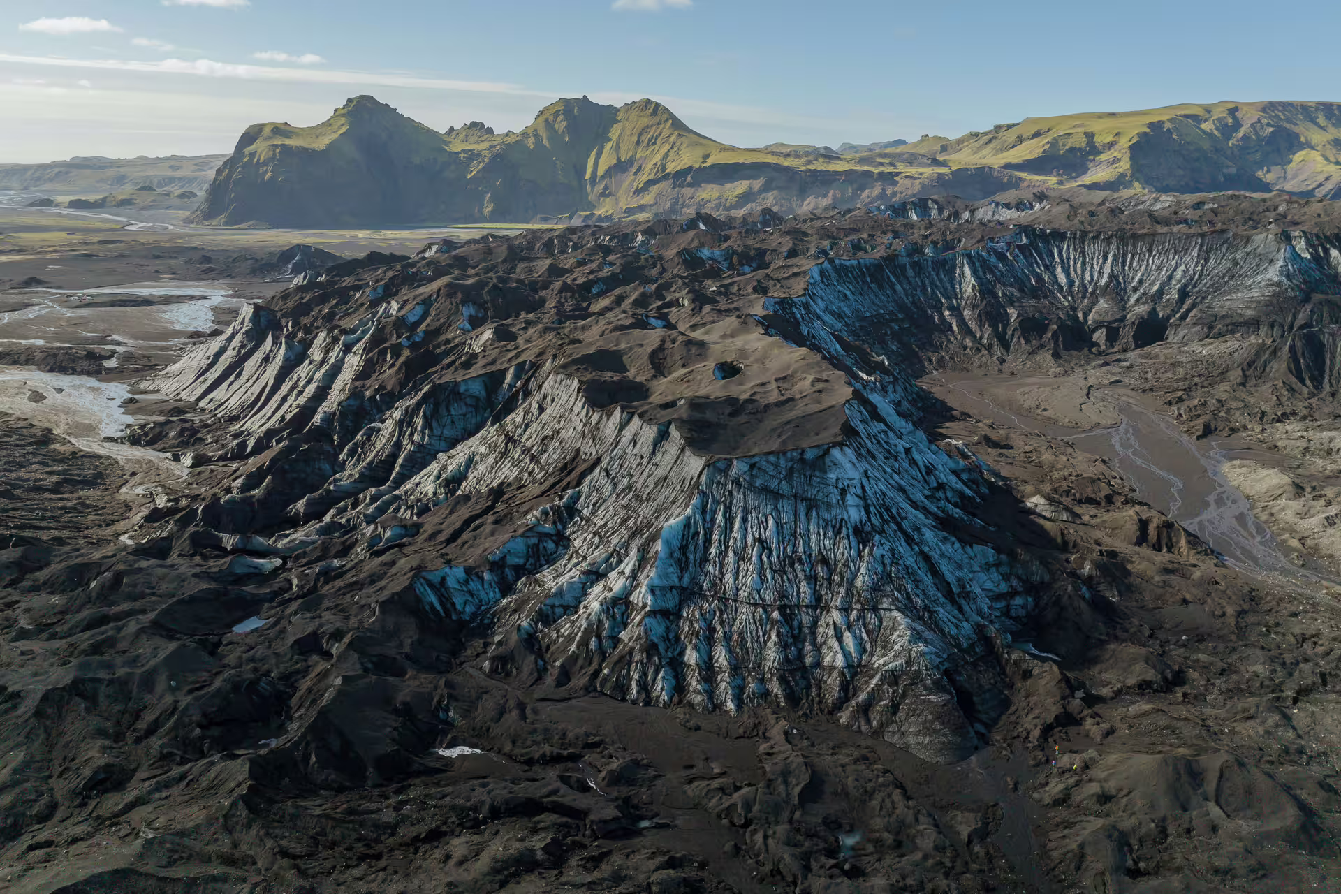 Aerial view of Katla glacier's striking blue ice formations layered with dark volcanic ash in Iceland's dramatic landscape.