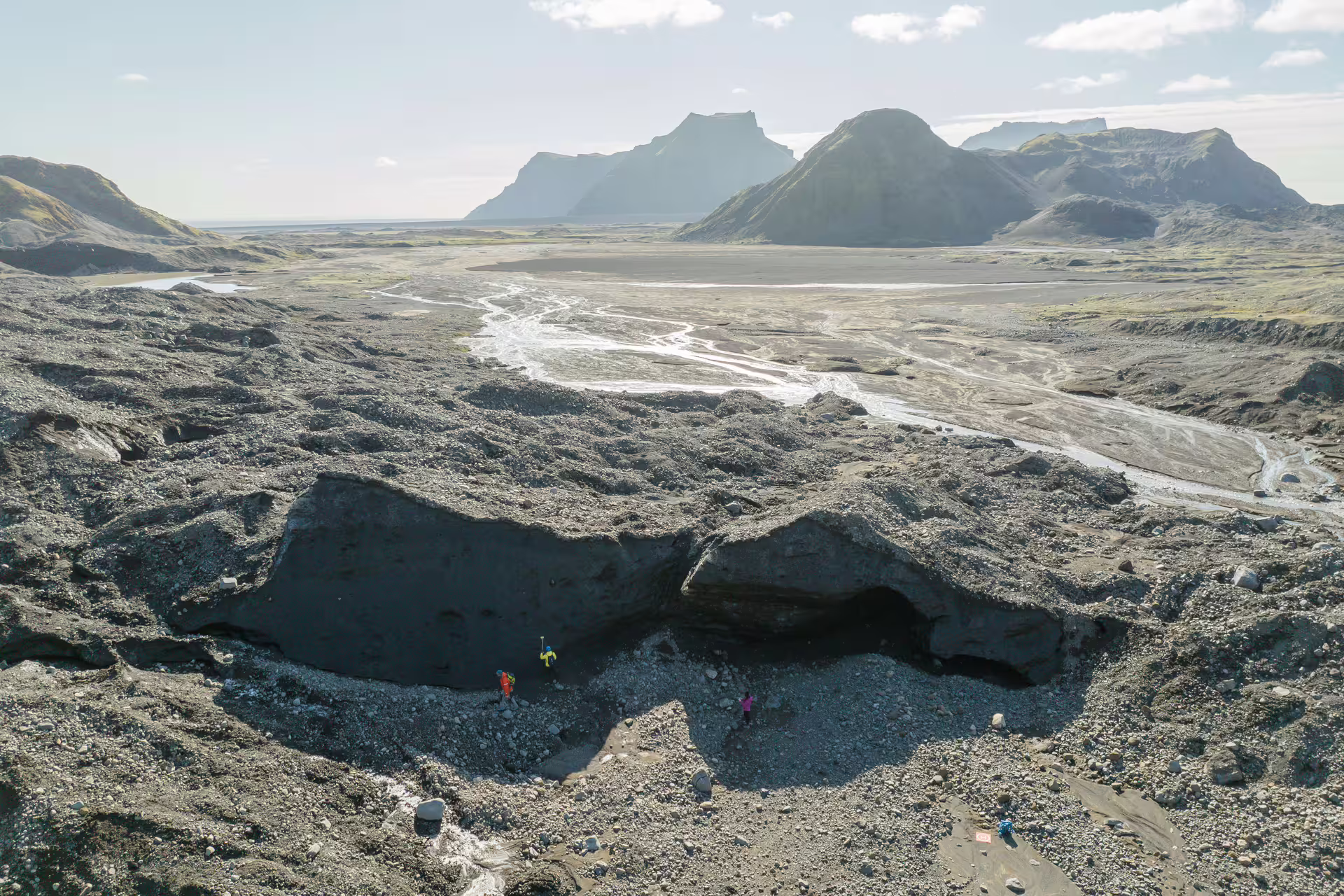 Aerial view of guides exploring dead ice sinkholes at Katla Glacier with volcanic black sand and braided rivers beyond