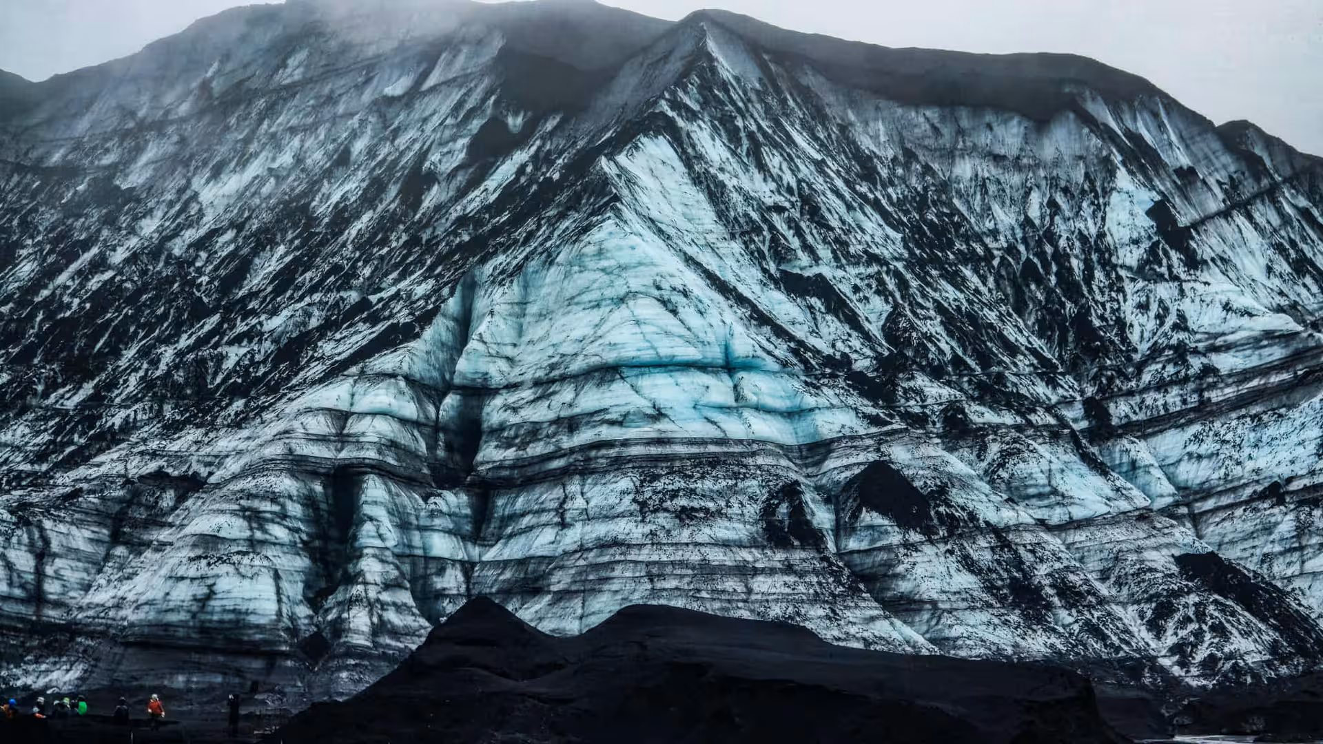 Black volcanic ash striped glacier ice cave wall at Katla volcano Iceland with tourists below