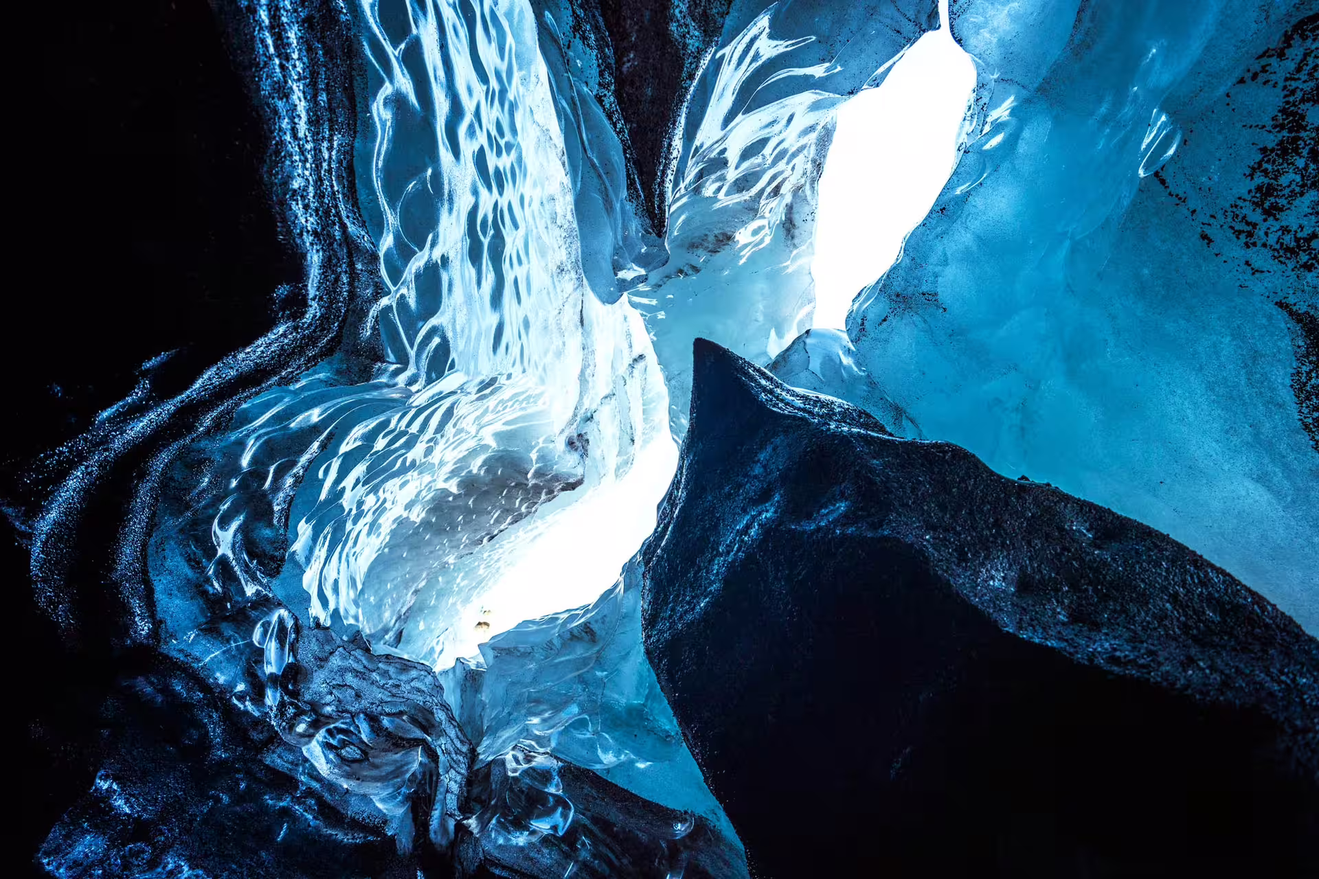 Glowing blue ice cave interior with black volcanic rock at Katla glacier, Iceland