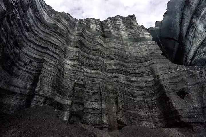 Dark layered ash and ice walls inside Katla ice cave viewed from below in Iceland