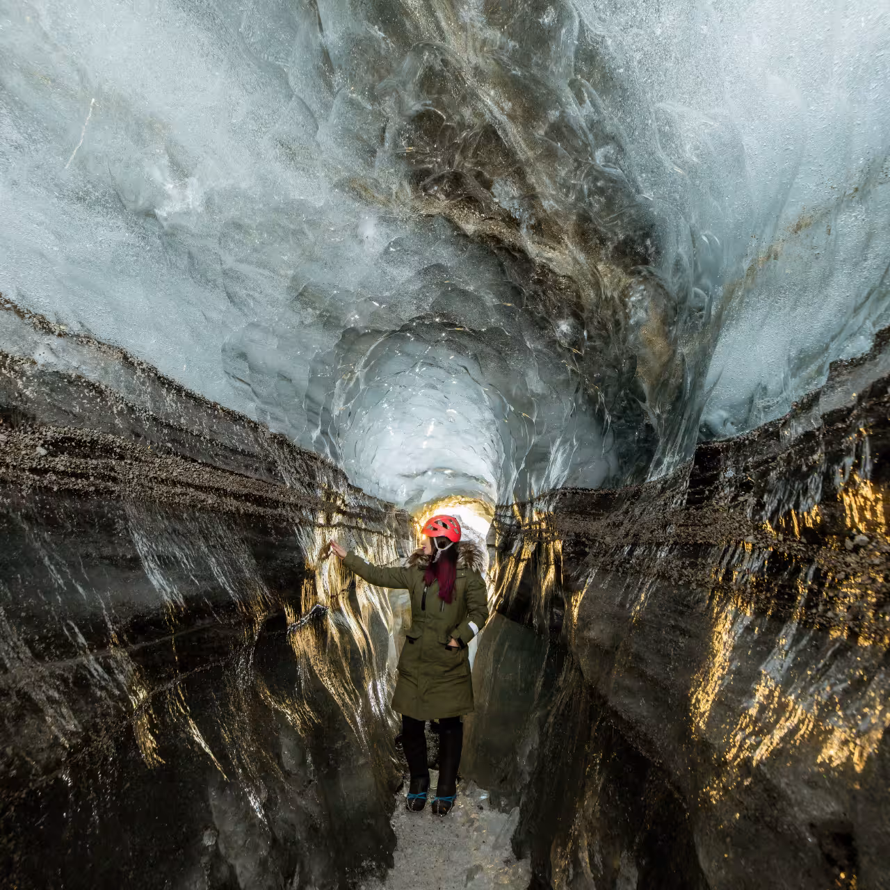 Explorer in red helmet inside Katla ice cave tunnel on Myrdalsjokull glacier day trip from Vik South Iceland