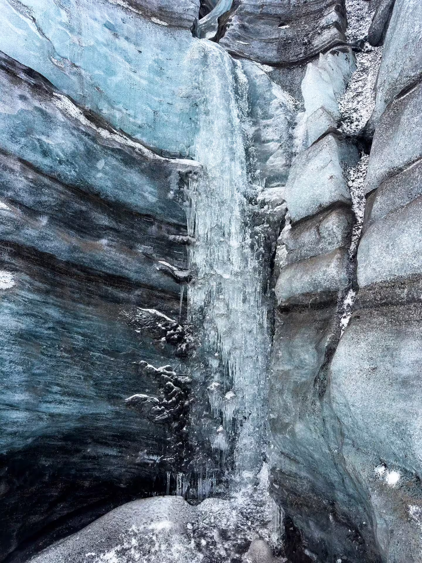 Stunning frozen icicle waterfall cascading down layered blue glacier walls inside Katla ice cave Iceland tour