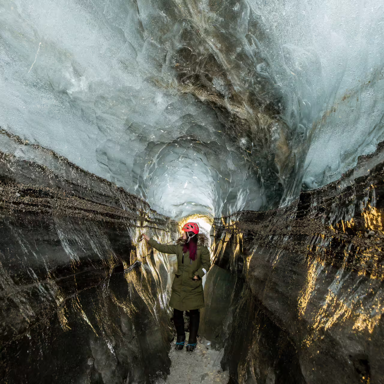 Tourist in safety helmet explores a stunning glacial ice tunnel on a Katla South Coast day trip from Reykjavik