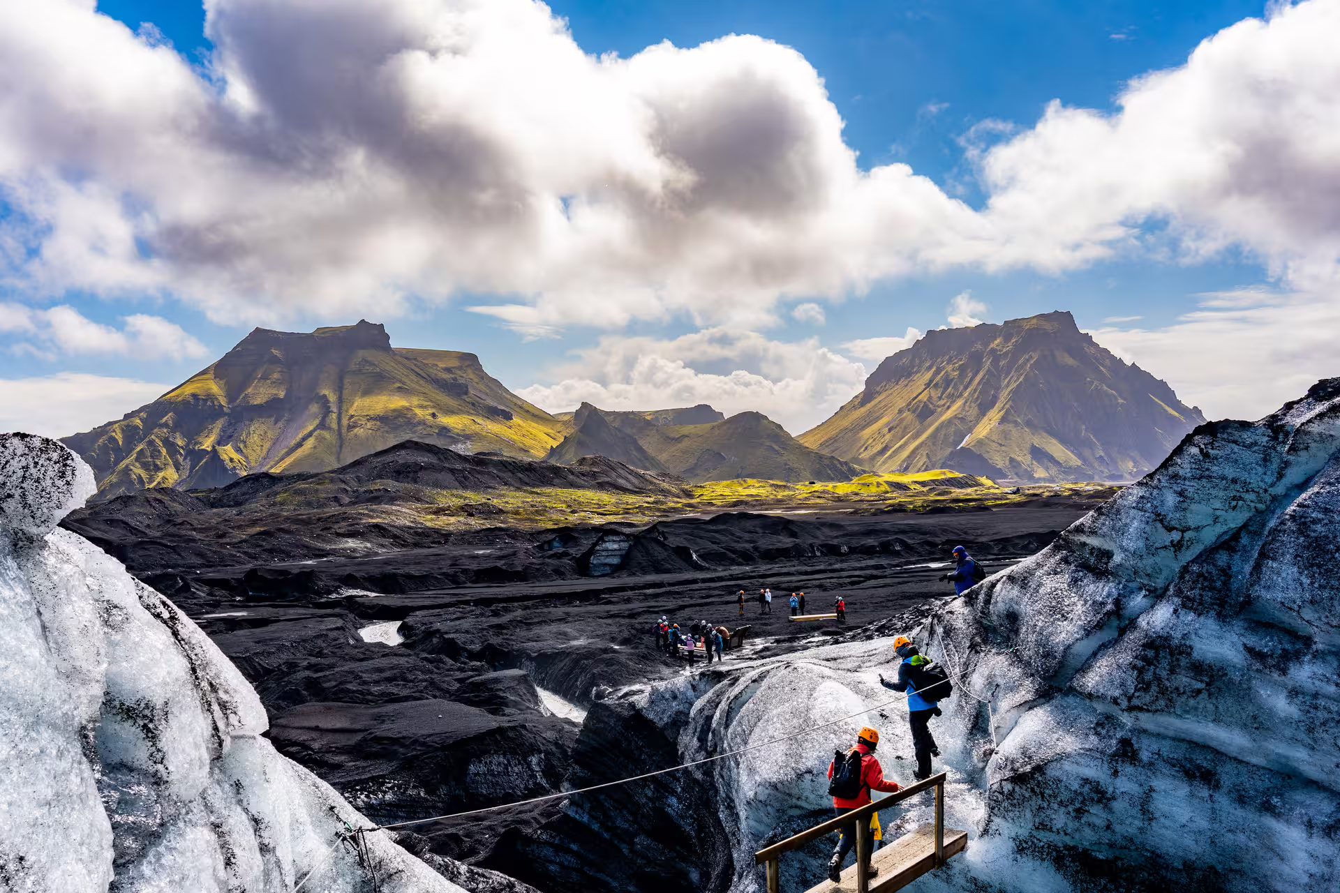 Tourists hiking on Katla glacier with black volcanic landscape and green mountains in Iceland