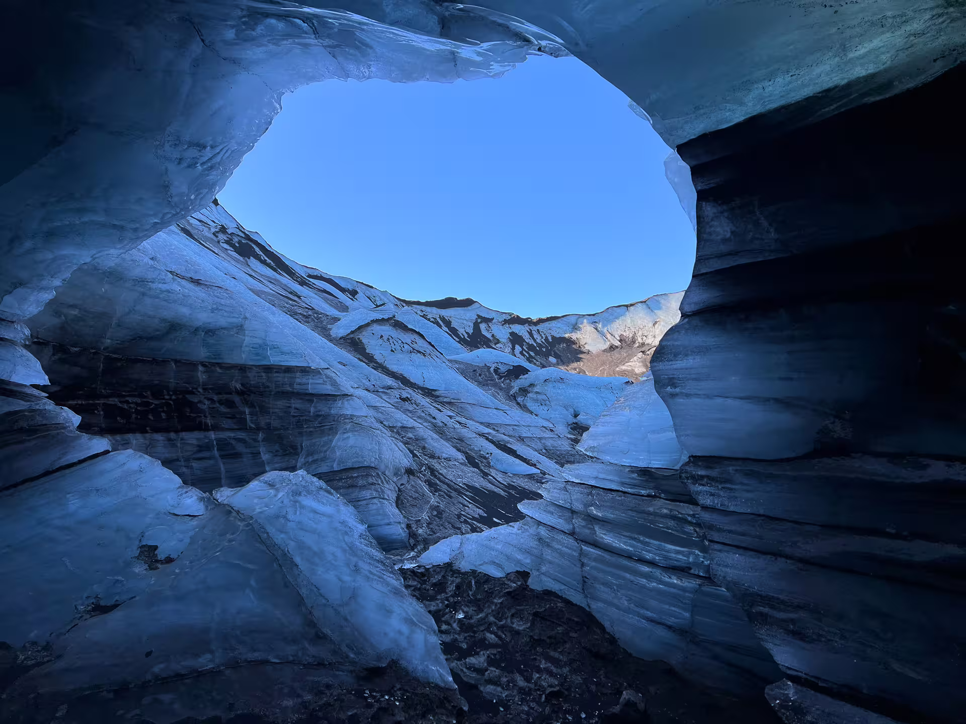 View from inside Katla ice cave looking out through oval opening to glacier and blue sky, Iceland
