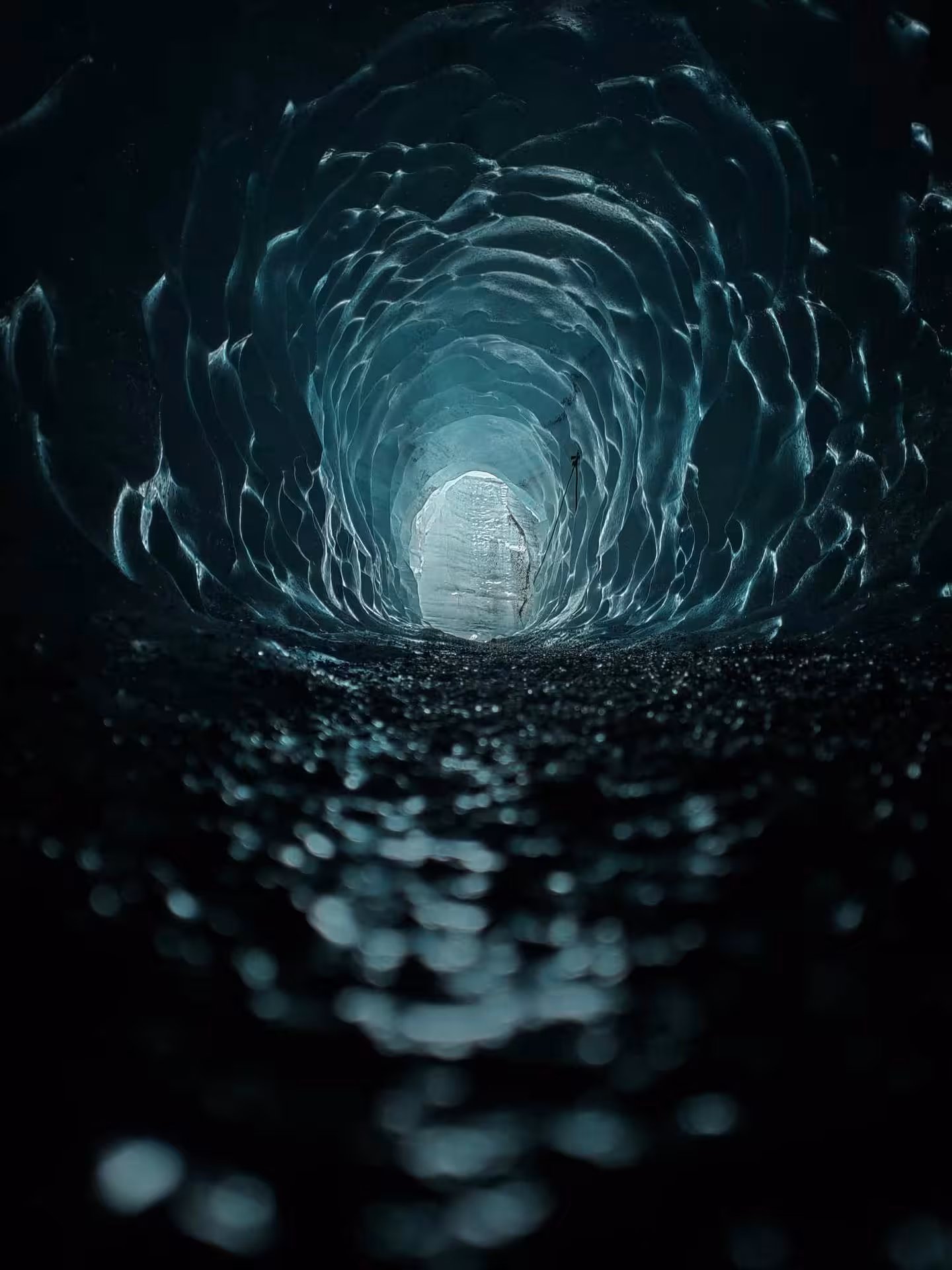 Glowing ice tunnel inside Katla volcano glacier cave with dark volcanic floor in Iceland