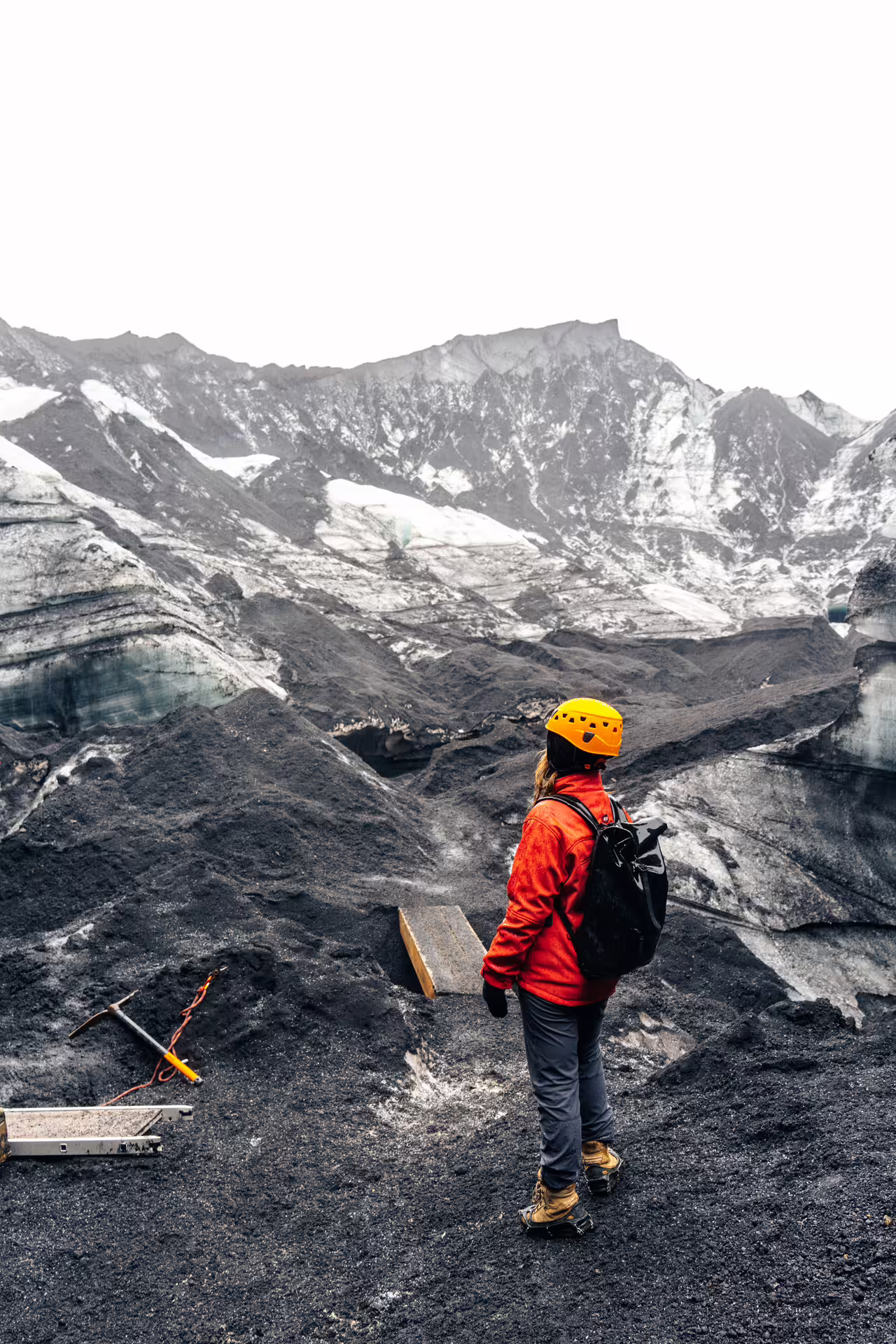 Hiker in red jacket and yellow helmet standing on black volcanic ash glacier at Katla Iceland