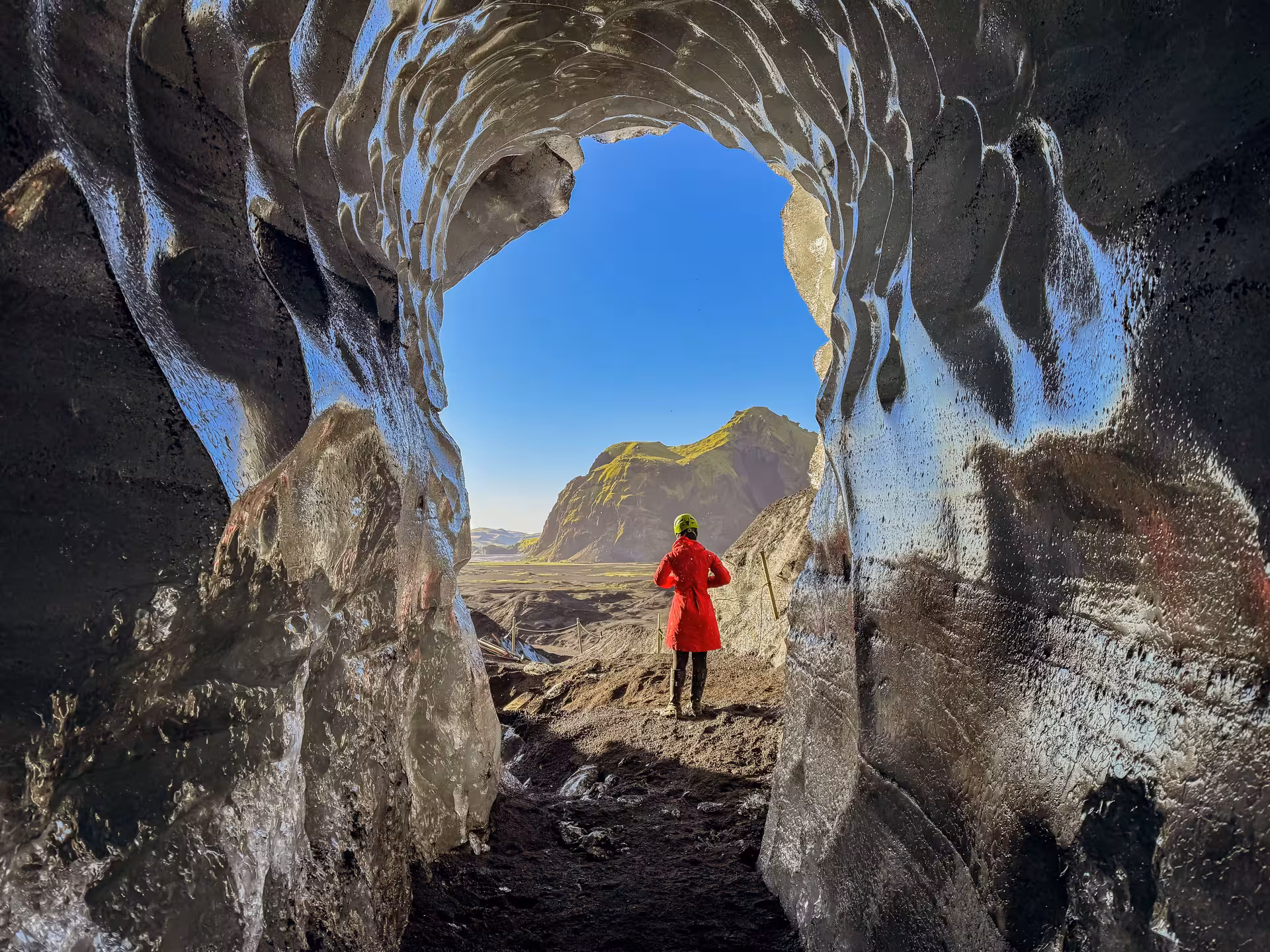A hiker in a red jacket stands at the stunning Katla ice cave entrance framing the Myrdalsjokull Glacier landscape near Vik Iceland.
