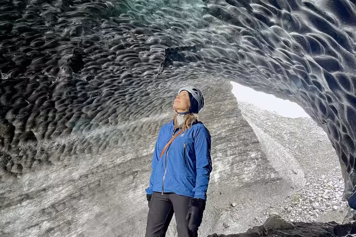 Two explorers gazing up at blue glacial ice cave ceiling at Katla volcano, Iceland