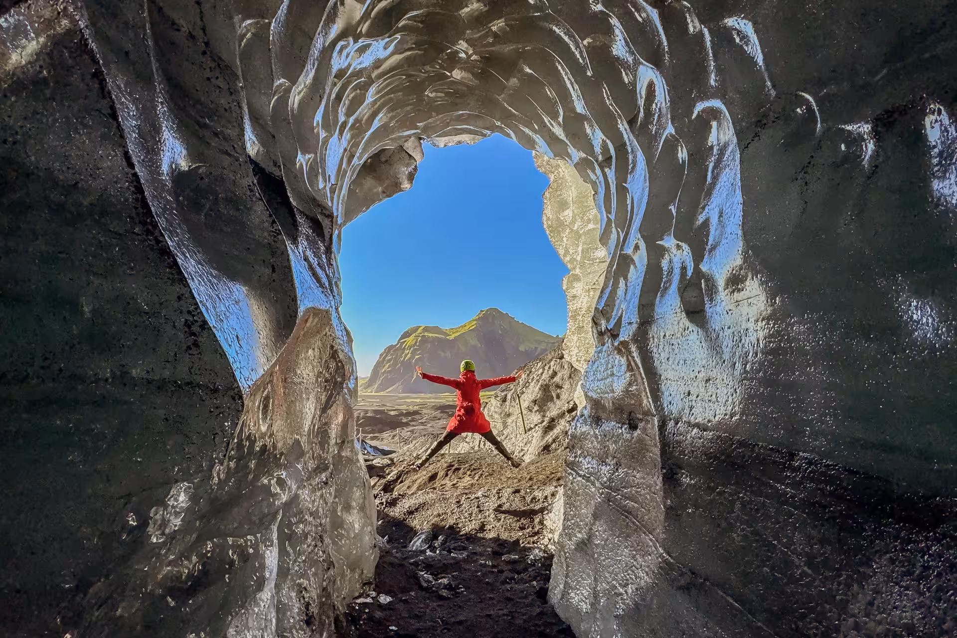 Excited traveler in red jacket jumping inside Katla ice cave with stunning Myrdalsjokull glacier views from Vik Iceland