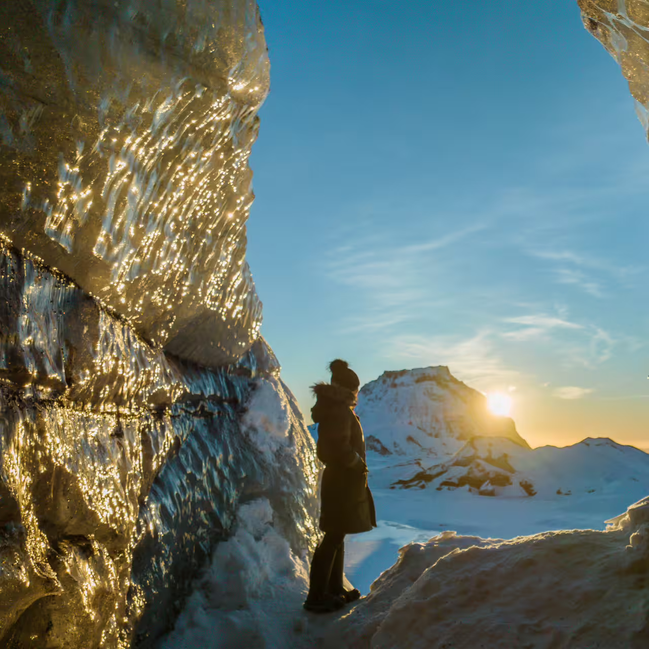 Traveler silhouetted inside sparkling Katla ice cave at golden sunset on Iceland South Coast day trip from Reykjavik