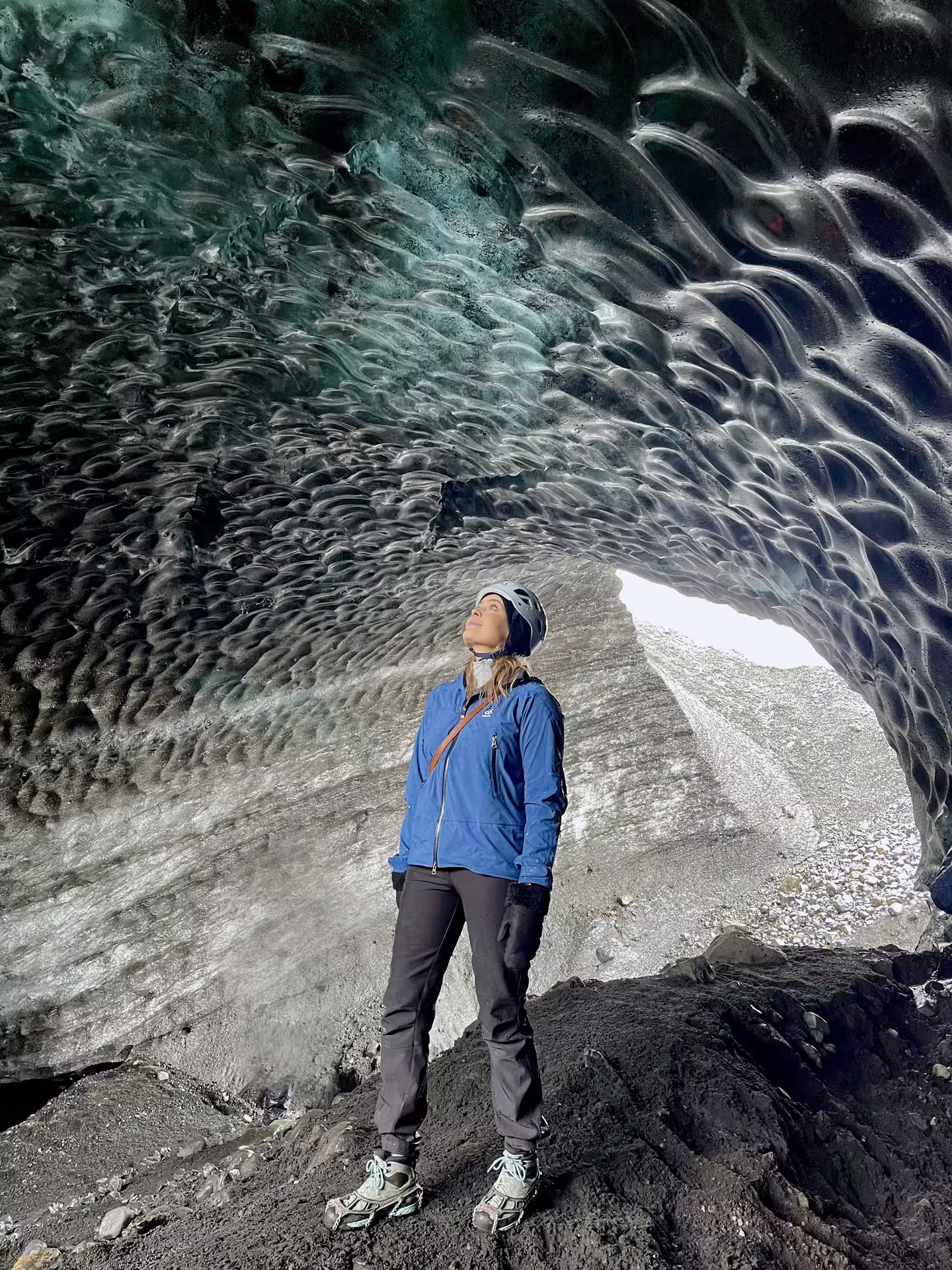 Woman in blue jacket gazing up at textured ice ceiling inside Katla ice cave, Iceland
