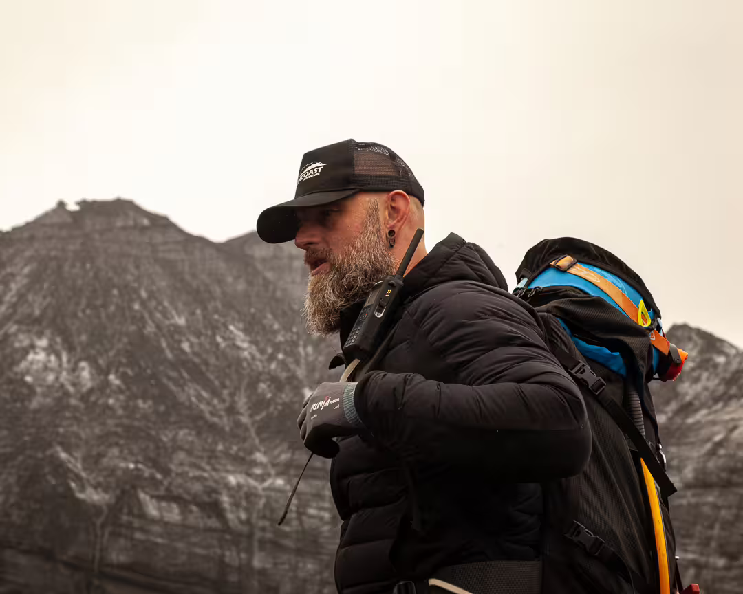 Bearded guide with backpack and radio in front of snow-dusted mountain on South Coast Iceland tour