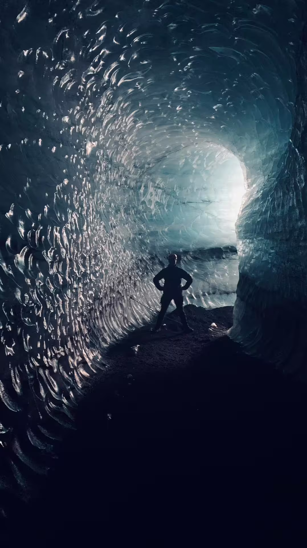 Silhouette of explorer standing inside Katla ice cave tunnel with glowing blue glacial walls