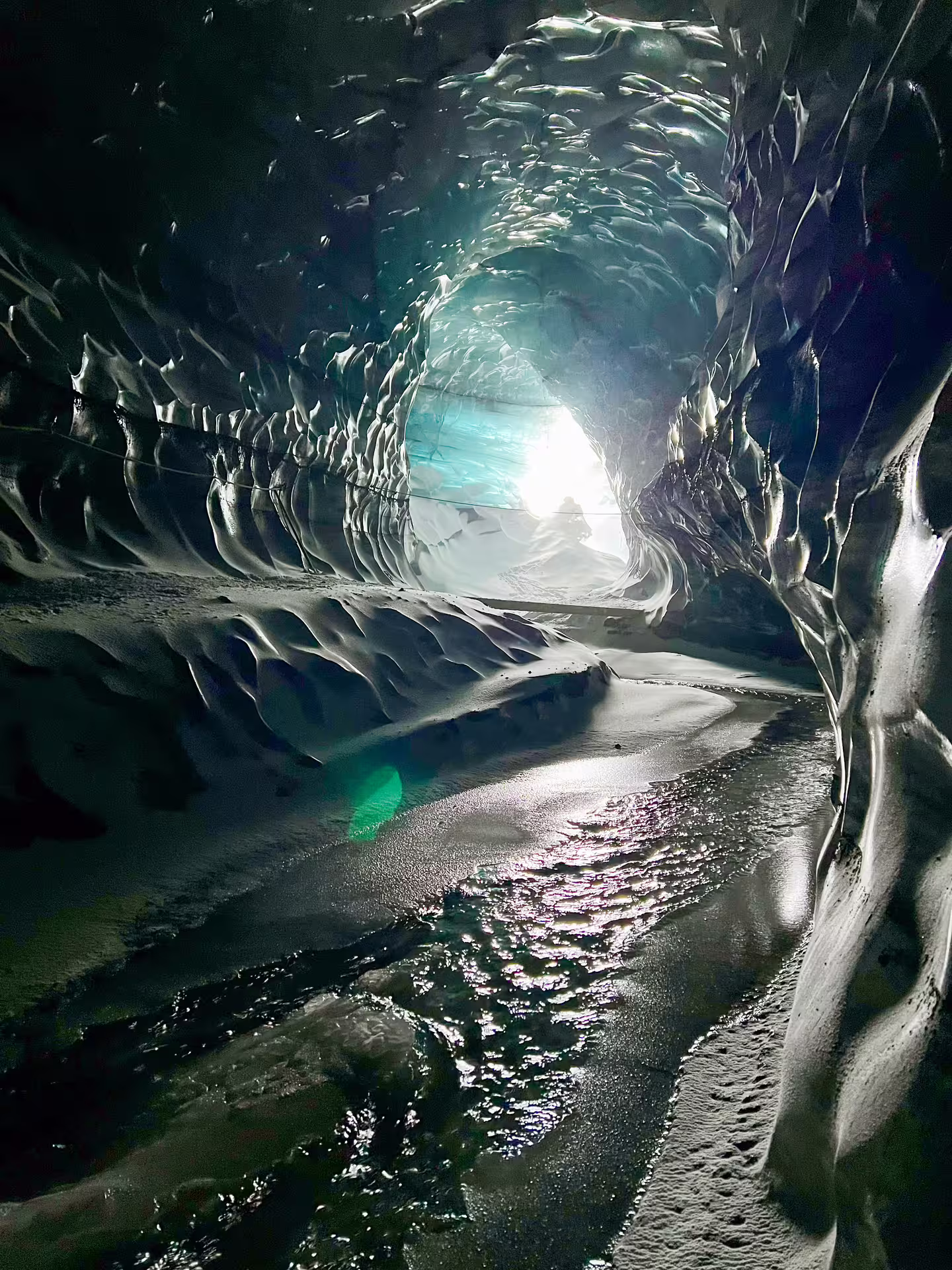 Glowing ice tunnel interior of Katla ice cave with meltwater stream and turquoise light, Iceland