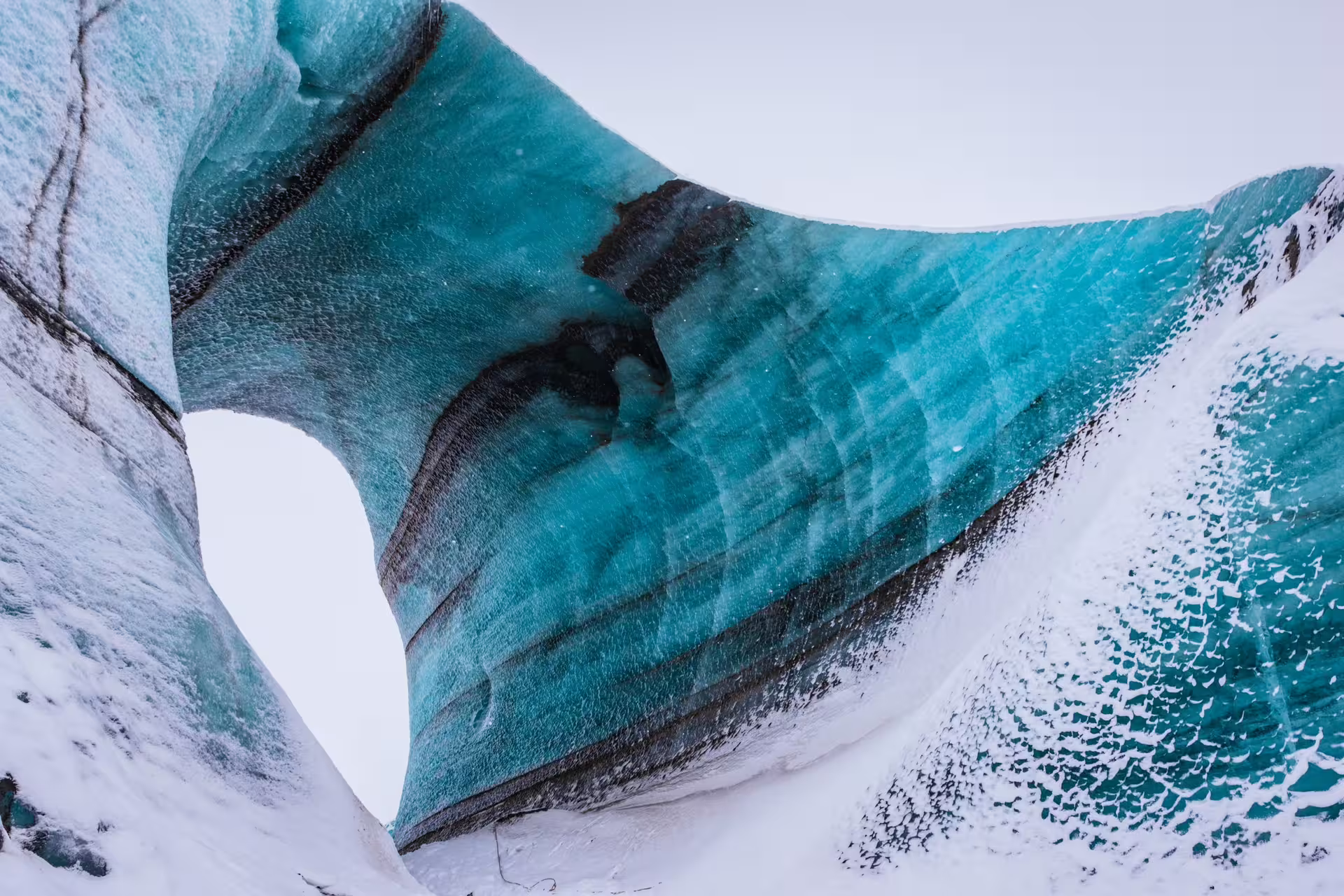 Vivid turquoise blue ice cave walls with dark volcanic streaks at Katla glacier, Iceland