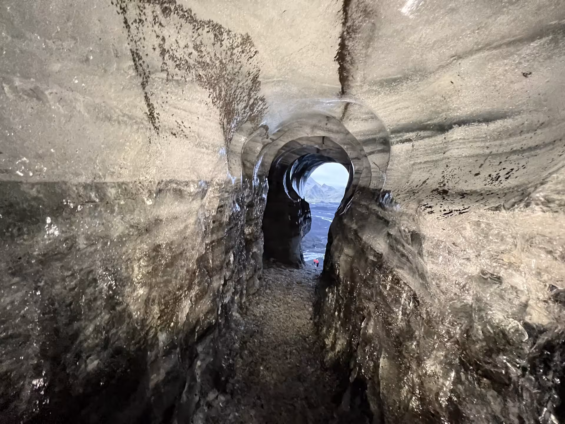 Tunnel inside Katla ice cave on Myrdalsjokull glacier revealing volcanic mountains through the icy arched opening