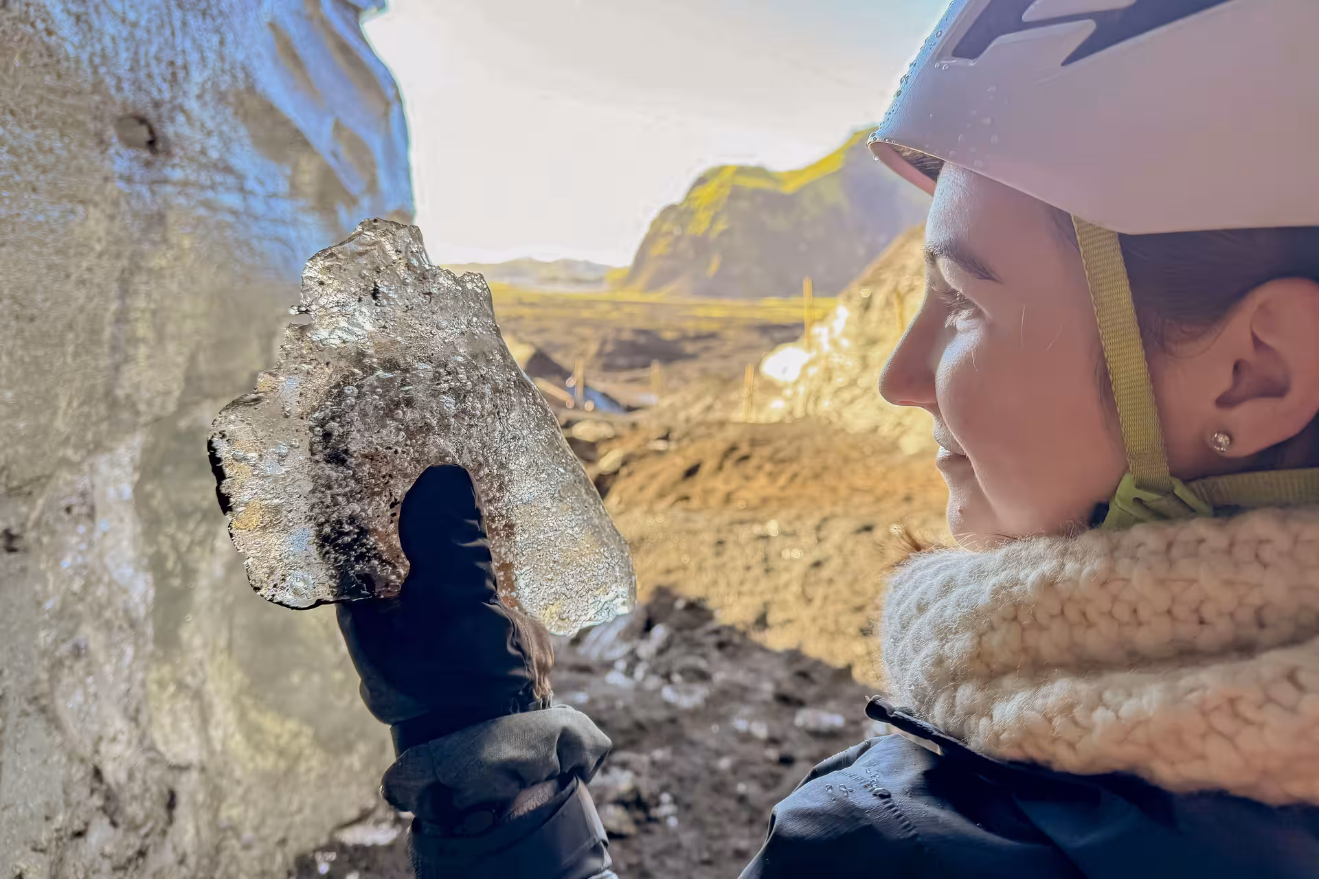 A helmeted visitor examines a volcanic ice chunk up close during a Katla ice cave day trip from Vik on Myrdalsjokull Glacier Iceland.