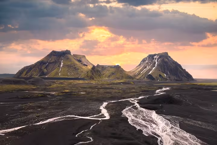 Black volcanic landscape with glacial river streams leading to green moss-covered mountains at sunset near Katla, Iceland