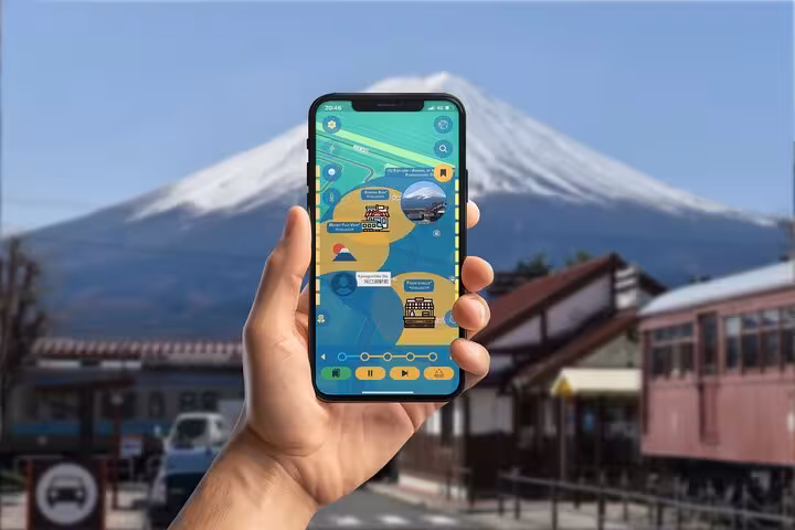 Hand holding smartphone with GPS city explorer app displaying Kawaguchiko map with Mount Fuji in background