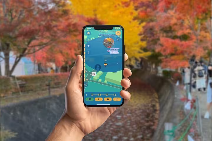 Hand holding smartphone with GPS city explorer app map near Kawaguchiko canal surrounded by autumn foliage