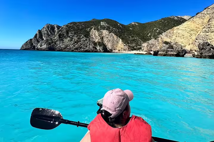 Kayaker explores the crystal-clear turquoise waters of Arrábida Natural Park in Sesimbra, surrounded by stunning cliffs.